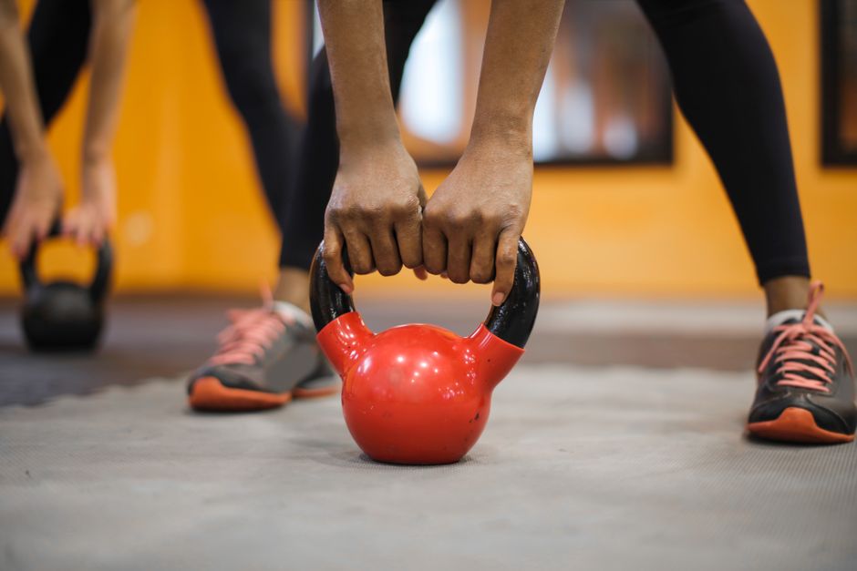 Hands gripping a red kettlebell in gym.