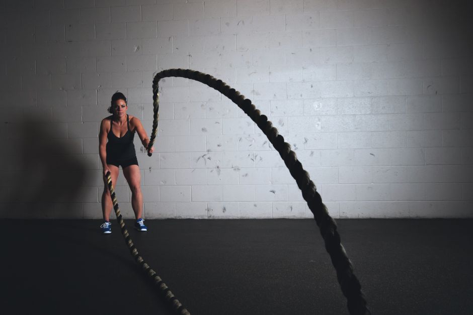 A focused woman performs a dynamic battle rope exercise in a gym setting.