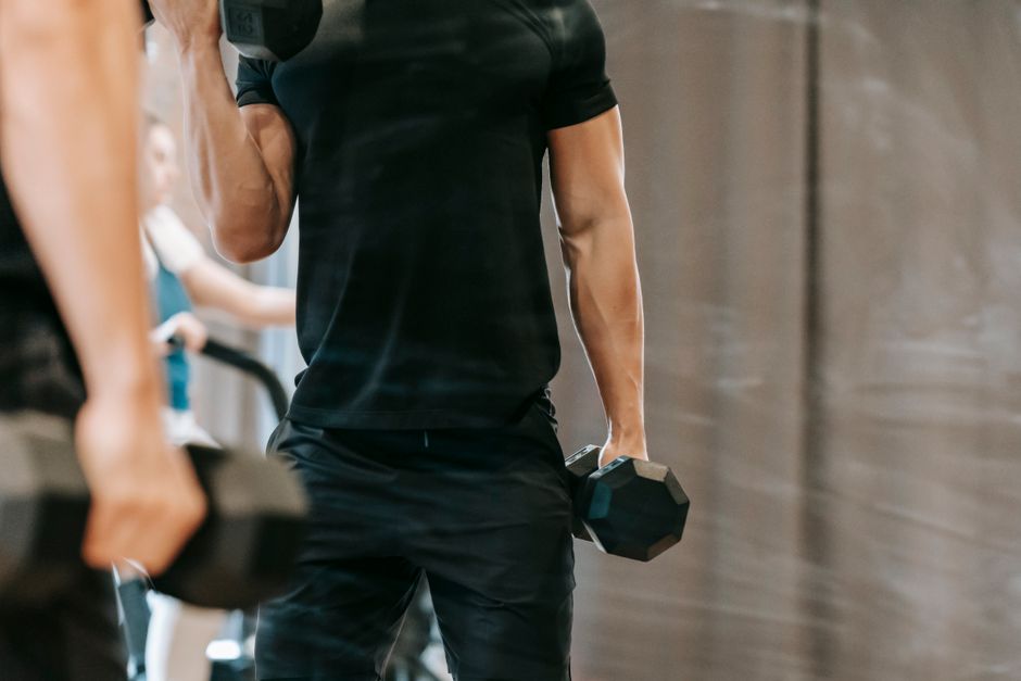 Muscular male lifting dumbbells in fitness studio.