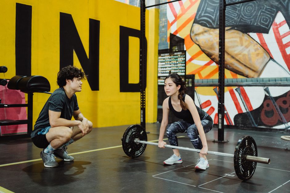 A young woman lifting weights guided by a trainer in a colorful gym setting